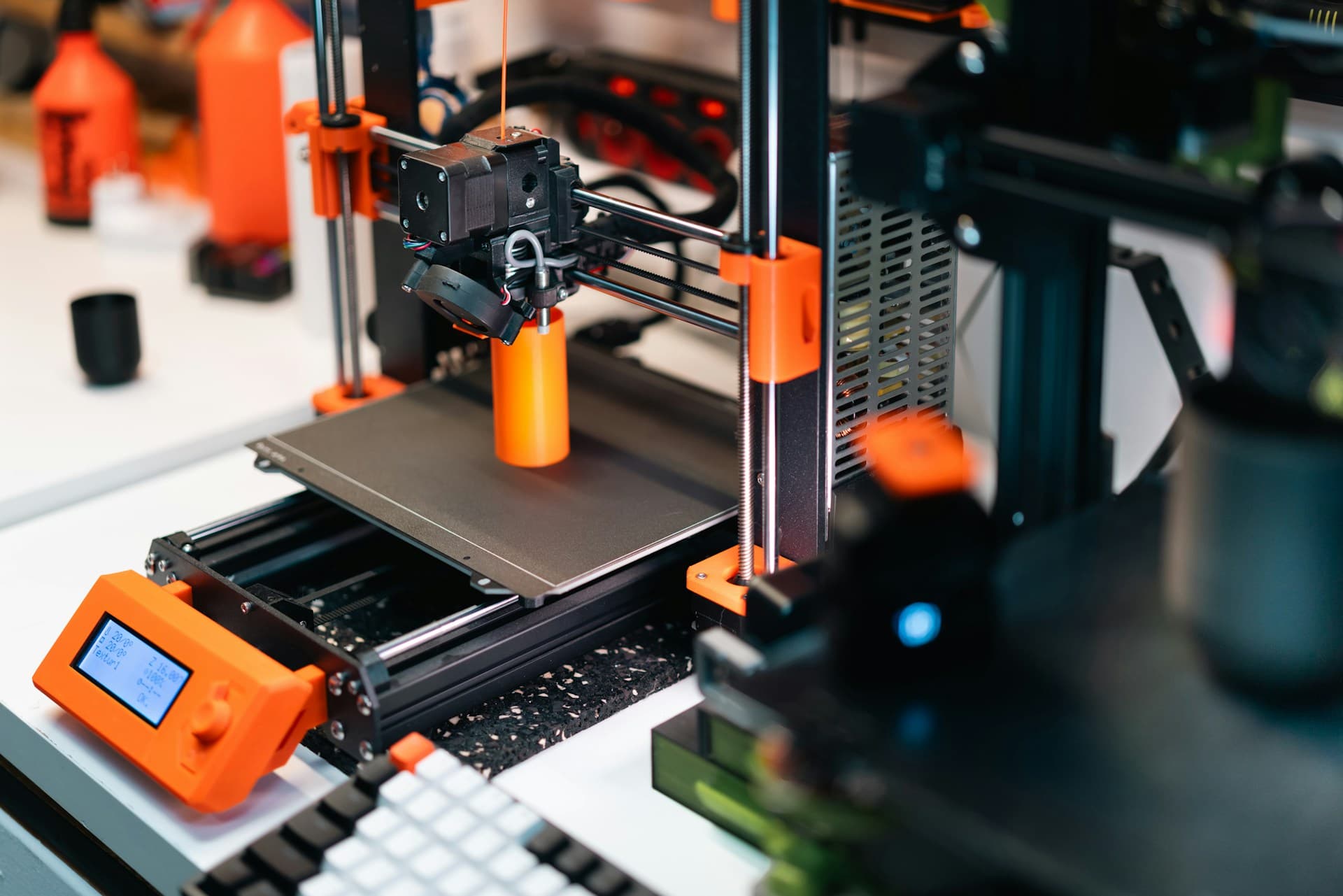 Desktop FDM 3D printer mid-print with an orange test part on the bed